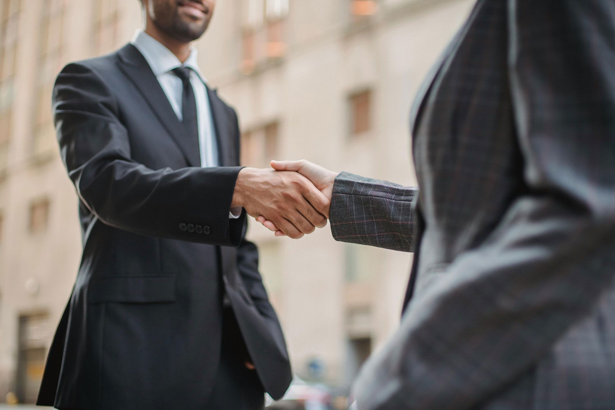 Two people in suits shaking hands outside a stone building